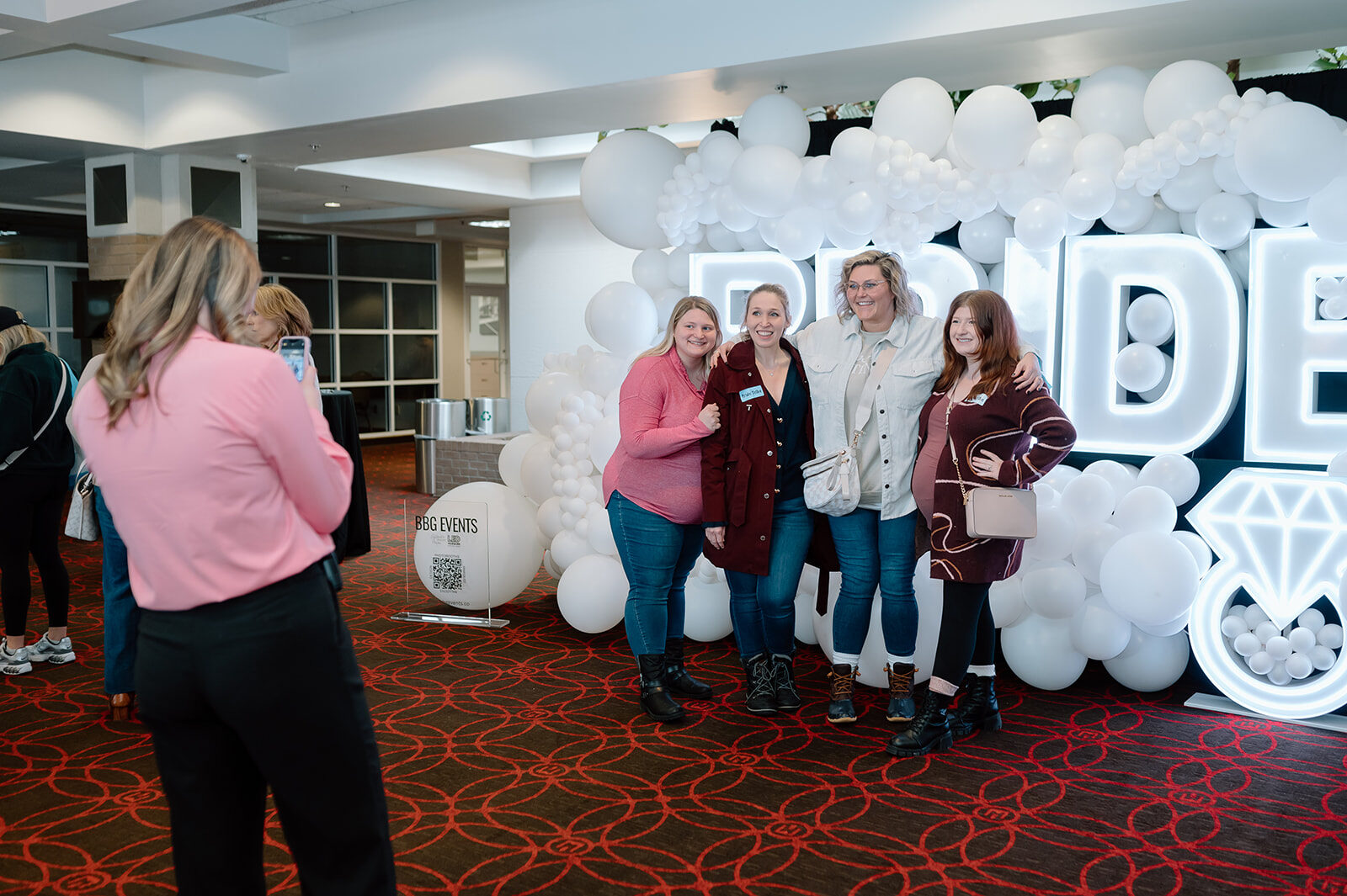 Four friends posing in front of a giant balloon wall spelling BRIDE